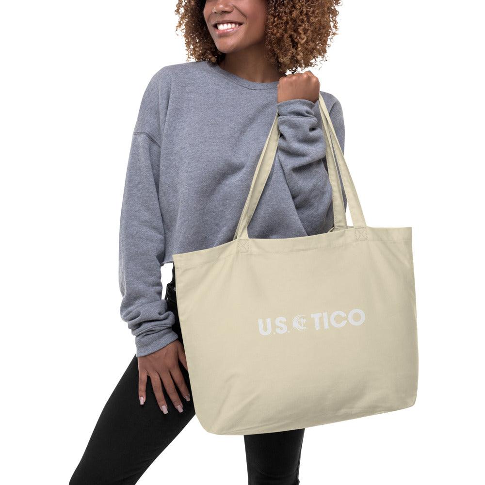 Woman wearing a grey sweatshirt holding a beige US TICO canvas tote bag.