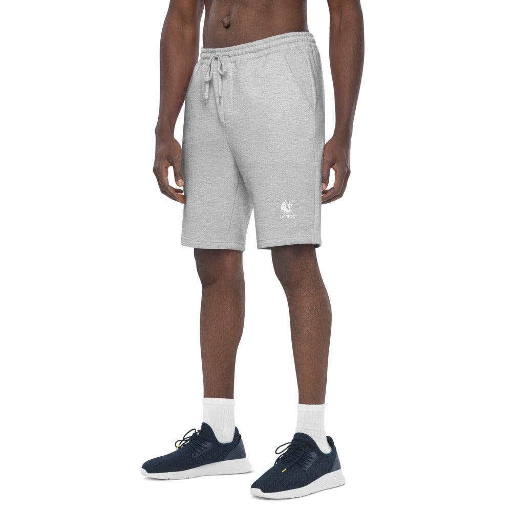 Man wearing grey drawstring sweat shorts with a small logo and navy blue sneakers